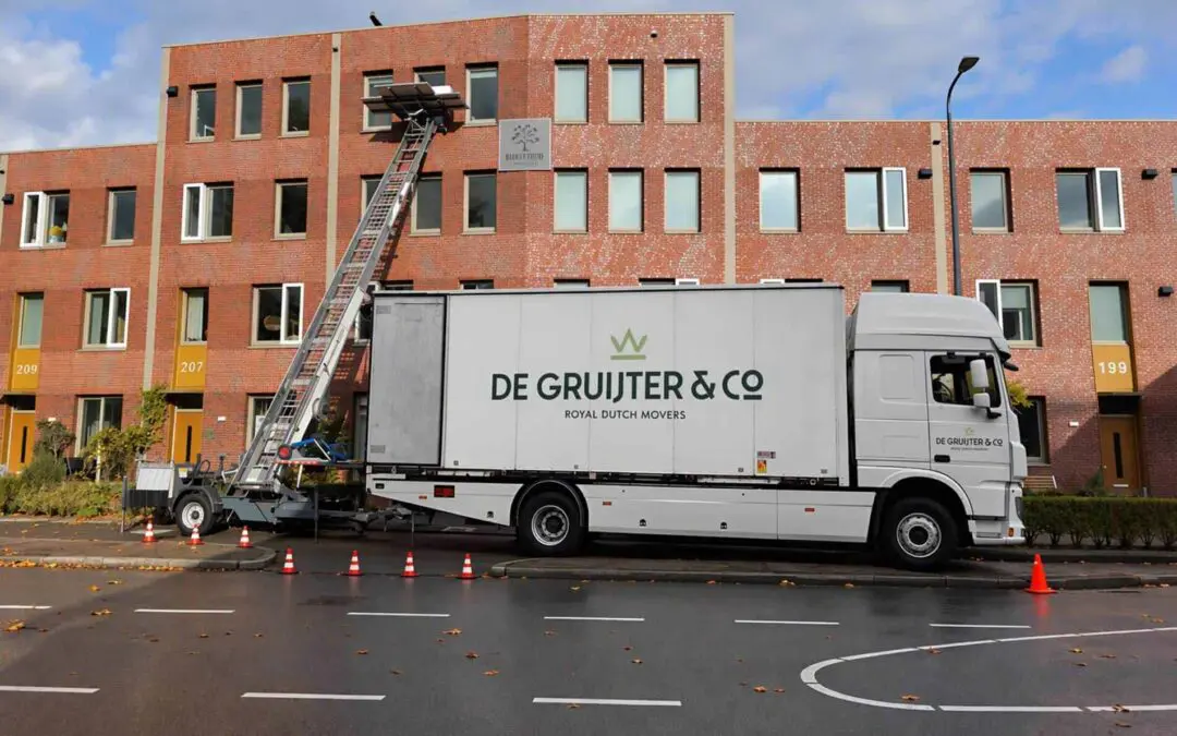 Verhuiswagen van De Gruijter & Co. met een verhuislift voor een bakstenen woongebouw.