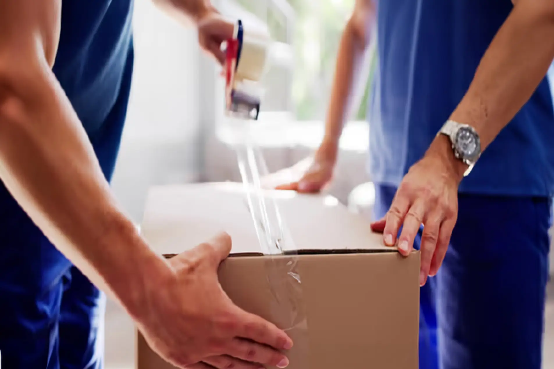 Twee professionele verhuizers sluiten een verhuisdoos met tape tijdens het inpakken van een inboedel voor een internationale verhuizing.