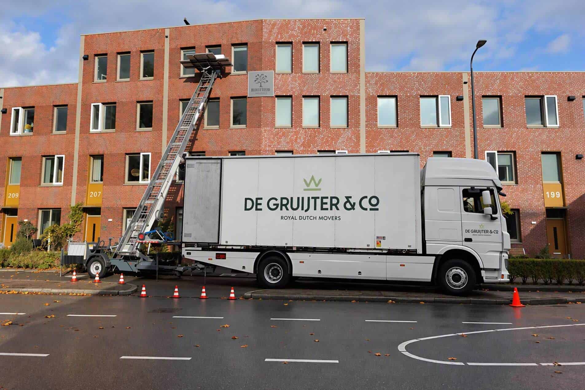 Verhuiswagen van De Gruijter & Co. met een verhuislift voor een bakstenen woongebouw.